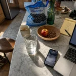 A kitchen counter with a glass of water, an apple with almonds, and a laptop in morning light, symbolizing healthy daily choices.
