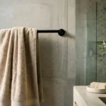 Beige bath towel hanging on a black towel bar beside a concrete sink with bar soap and a potted plant in a modern bathroom.